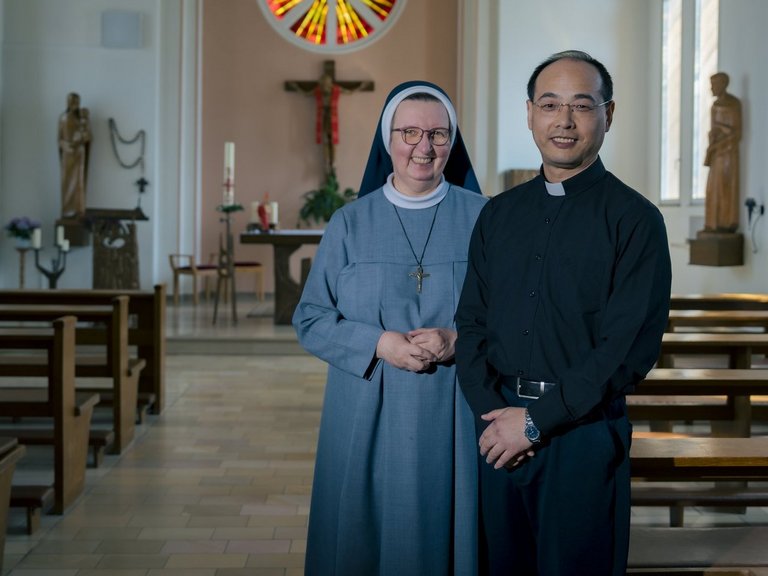 Der Hausgeistliche und eine Ordensschwester stehen in der Hauskapelle und lächeln in die Kamera.