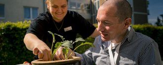 Junge Pflege Rheine Eine Mitarbeitende bepflanzt gemeinsam mit einem Bewohner einen Blumentopf.