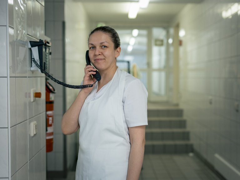 Eine Mitarbeitende hält den Telefonhörer ans Ohr und lächelt in die Kamera.